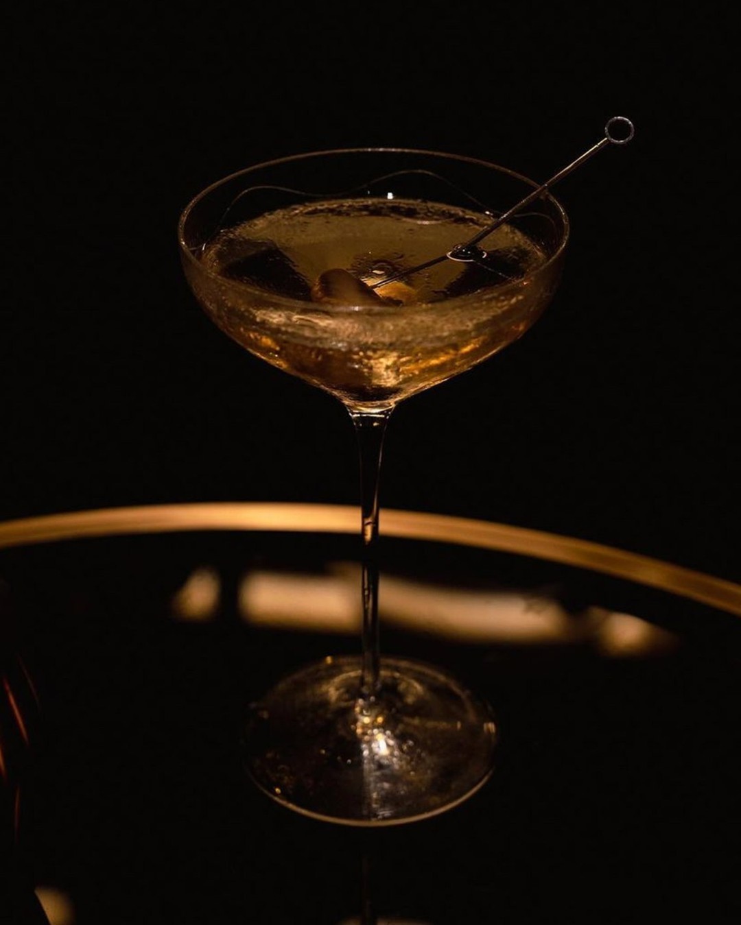 Coupe cocktail with olive pick against dark background