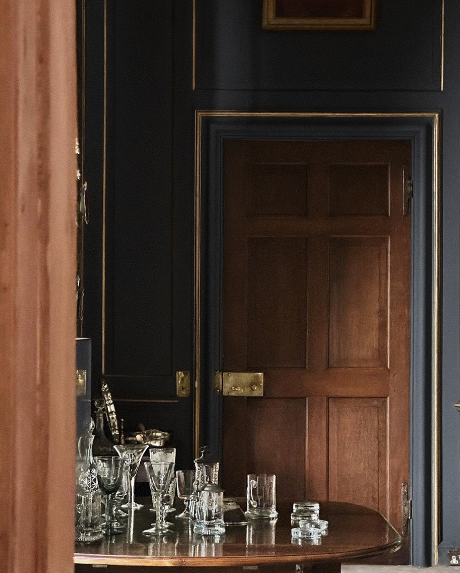 Crystal glassware on table in dark panelled room with oak door